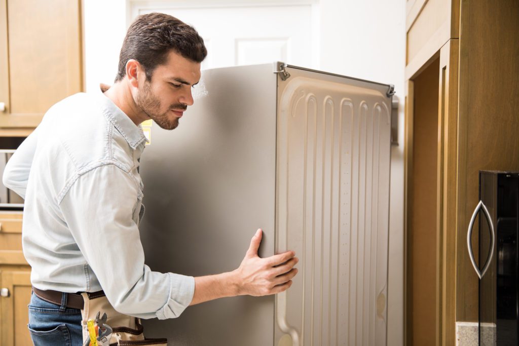 jovem trabalhando como eletricista expondo parte de trás de uma geladeira para verificar e repará la