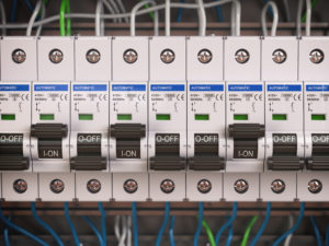 Disjuntores elétricos alinhados em um painel de distribuição, com cabos coloridos conectados ao fundo.