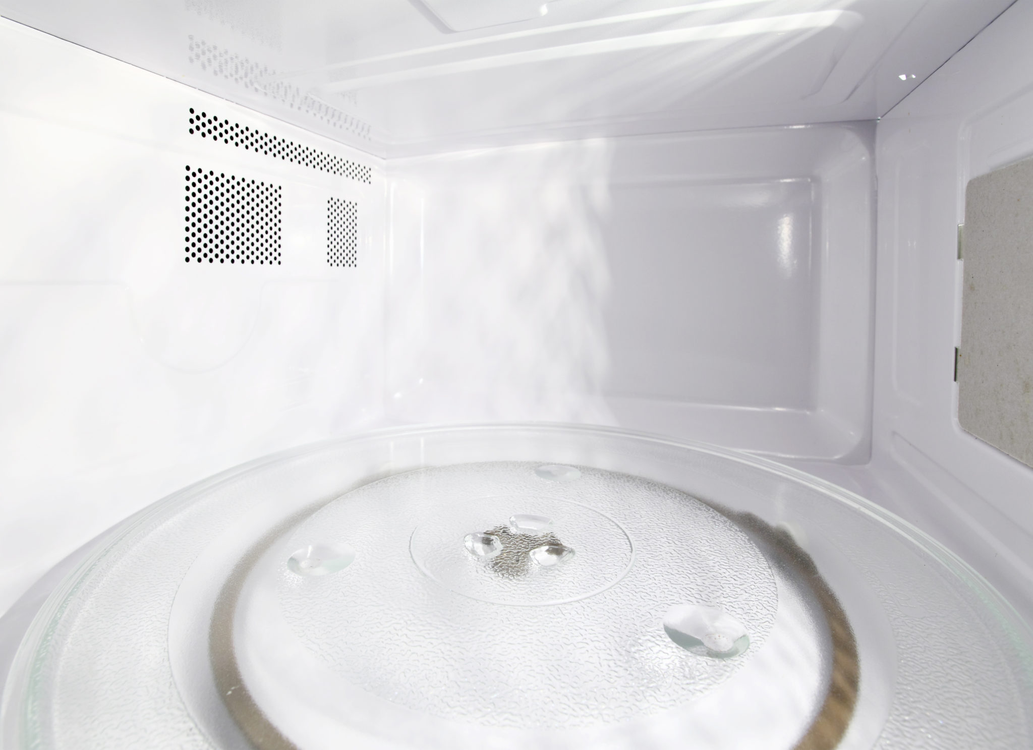 Interior de um micro-ondas limpo e vazio, com prato giratório de vidro e gotas de água sobre a superfície.