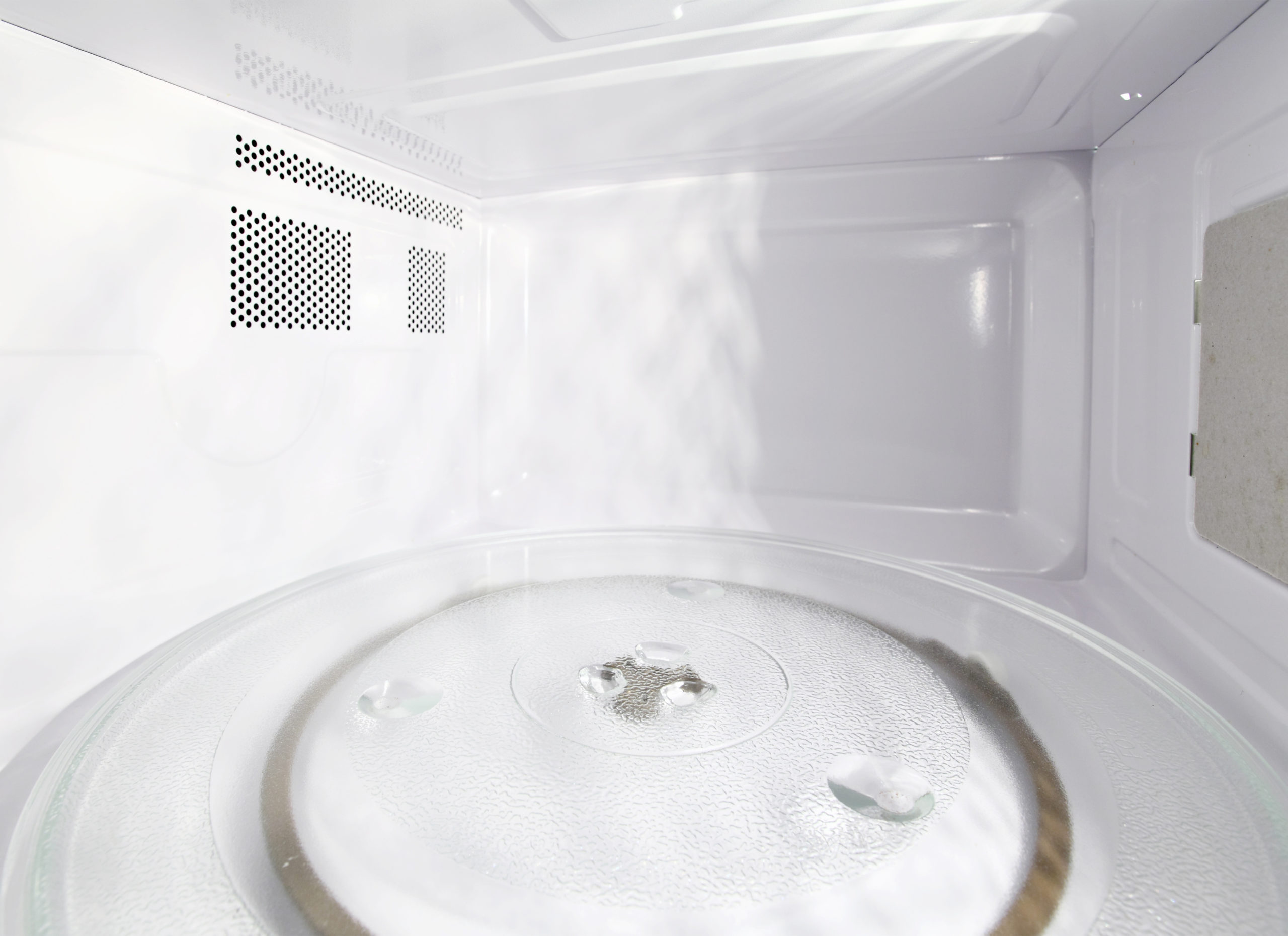 Interior de um micro-ondas limpo e vazio, com prato giratório de vidro e gotas de água sobre a superfície.