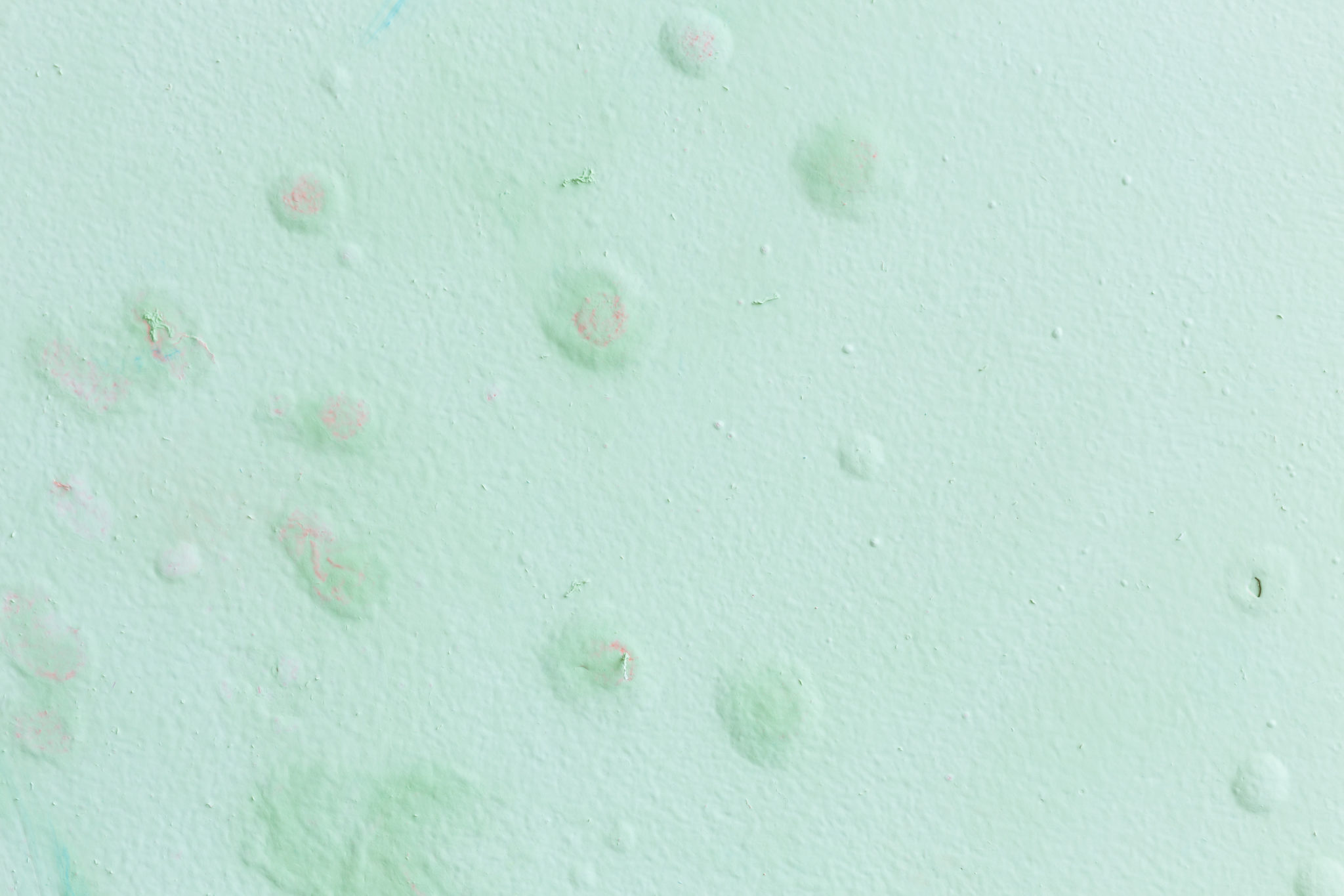 Parede verde-clara com textura irregular, pequenas bolhas, descascados e manchas suaves em tons de rosa e azul