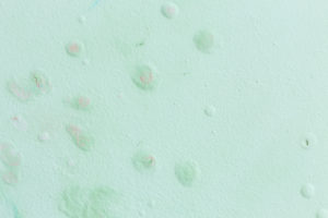 Parede verde-clara com textura irregular, pequenas bolhas, descascados e manchas suaves em tons de rosa e azul