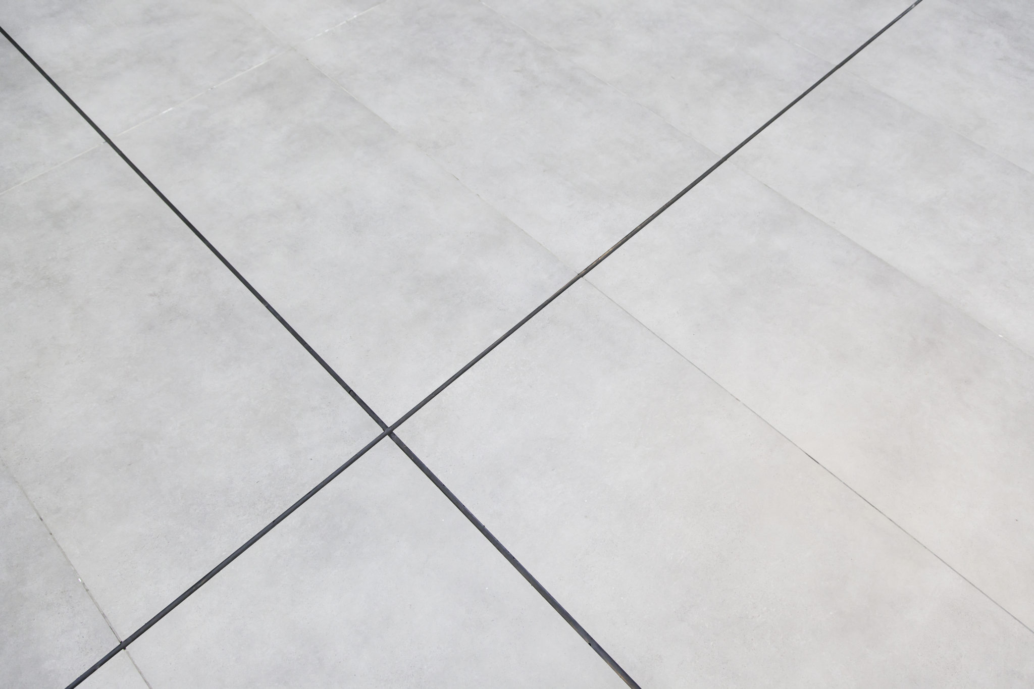 Piso de porcelanato cinza claro com rejuntes escuros formando linhas diagonais e um padrão geométrico abstrato.
