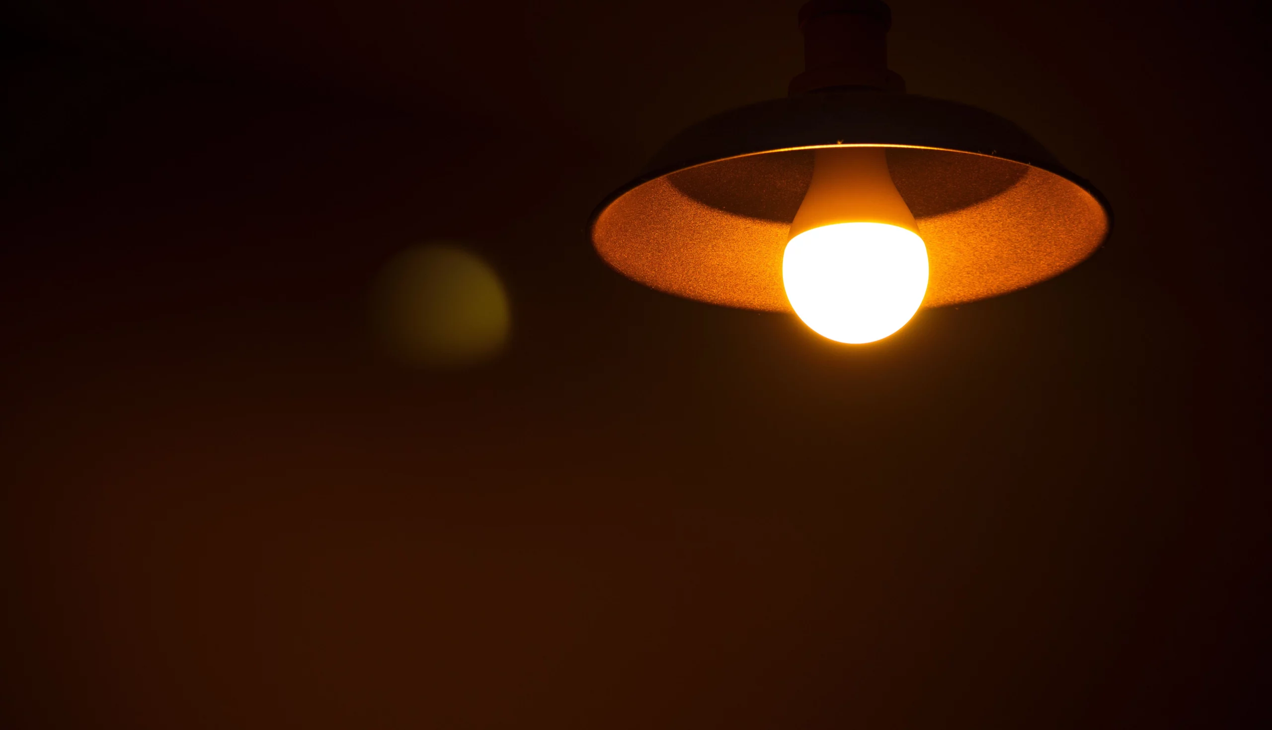 Lâmpada acesa pendurada em um ambiente escuro, emitindo luz quente e criando uma atmosfera intimista.