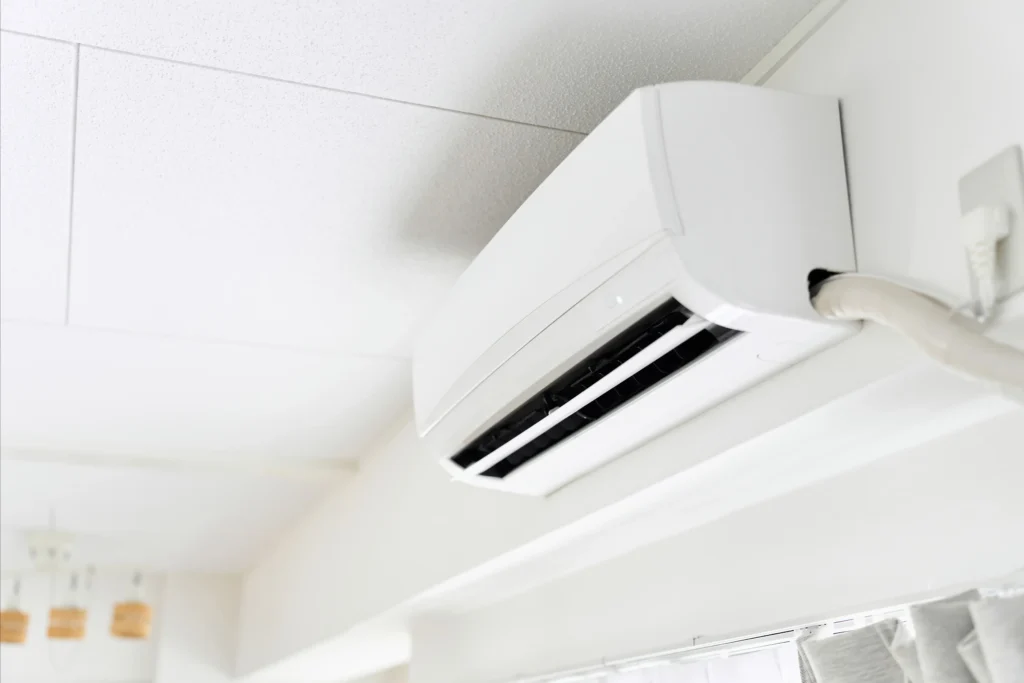 Ar-condicionado split branco instalado na parede de um ambiente interno, com saída de ar direcionada para o cômodo e decoração em tons claros ao fundo.