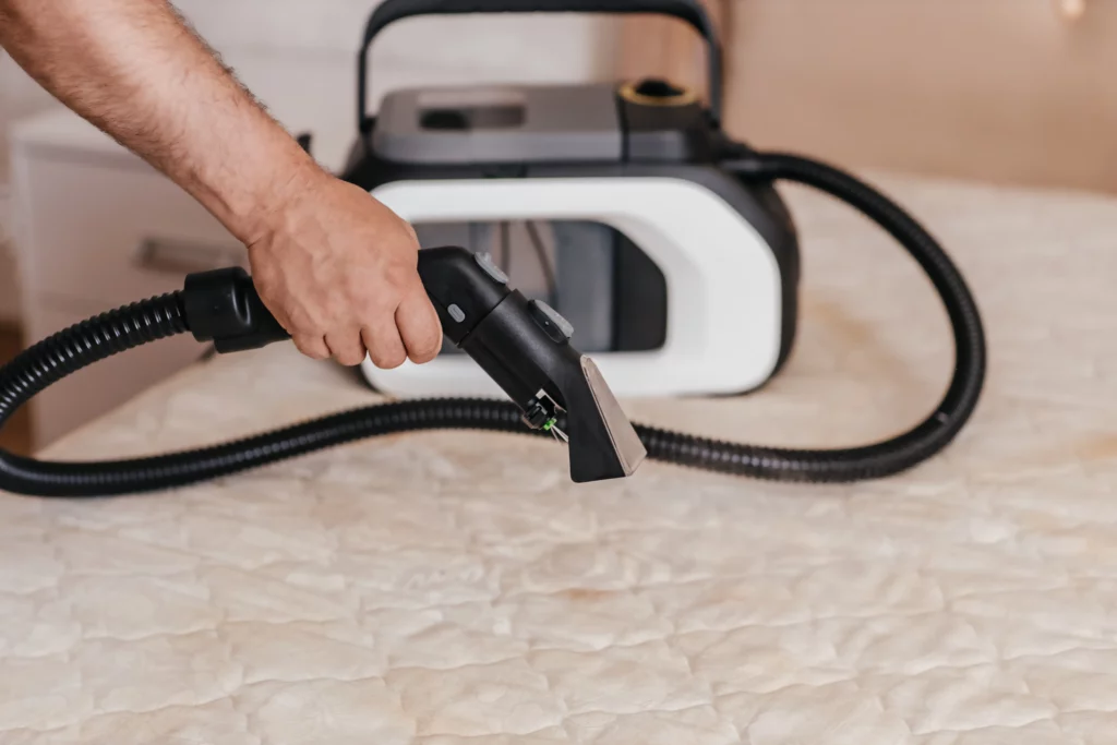 Pessoa utilizando uma máquina extratora para higienizar e limpar um colchão branco.
