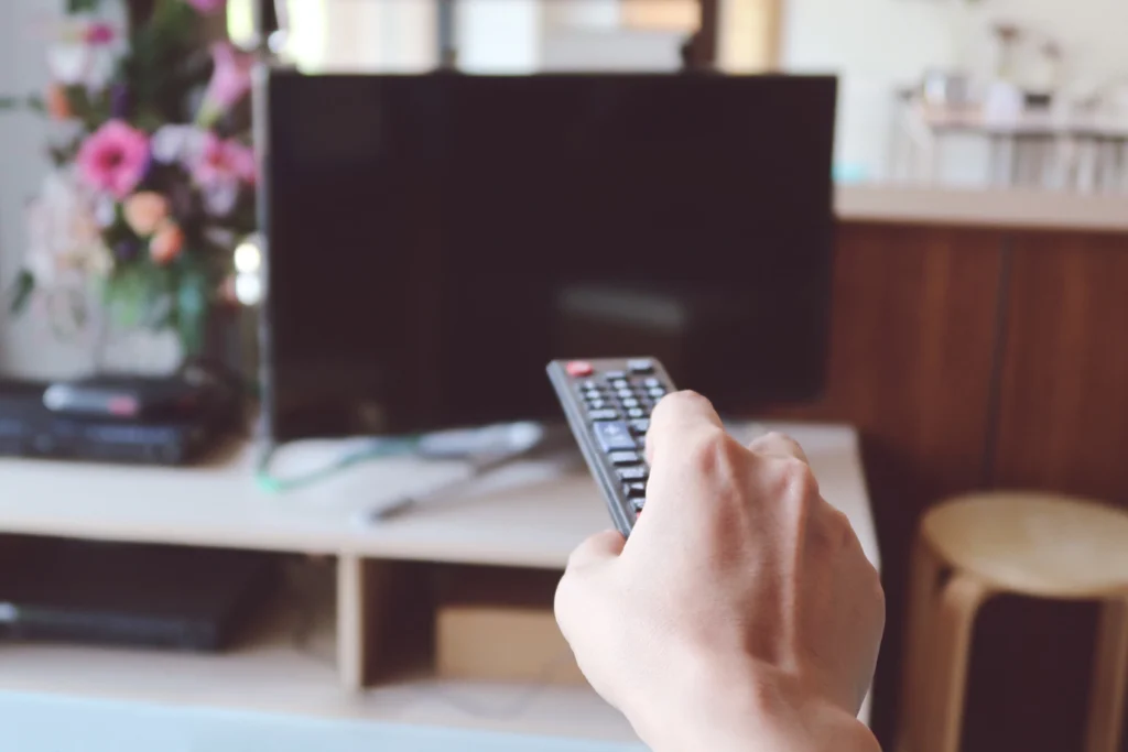 Pessoa segurando um controle remoto em direção a uma televisão desligada em uma sala de estar.