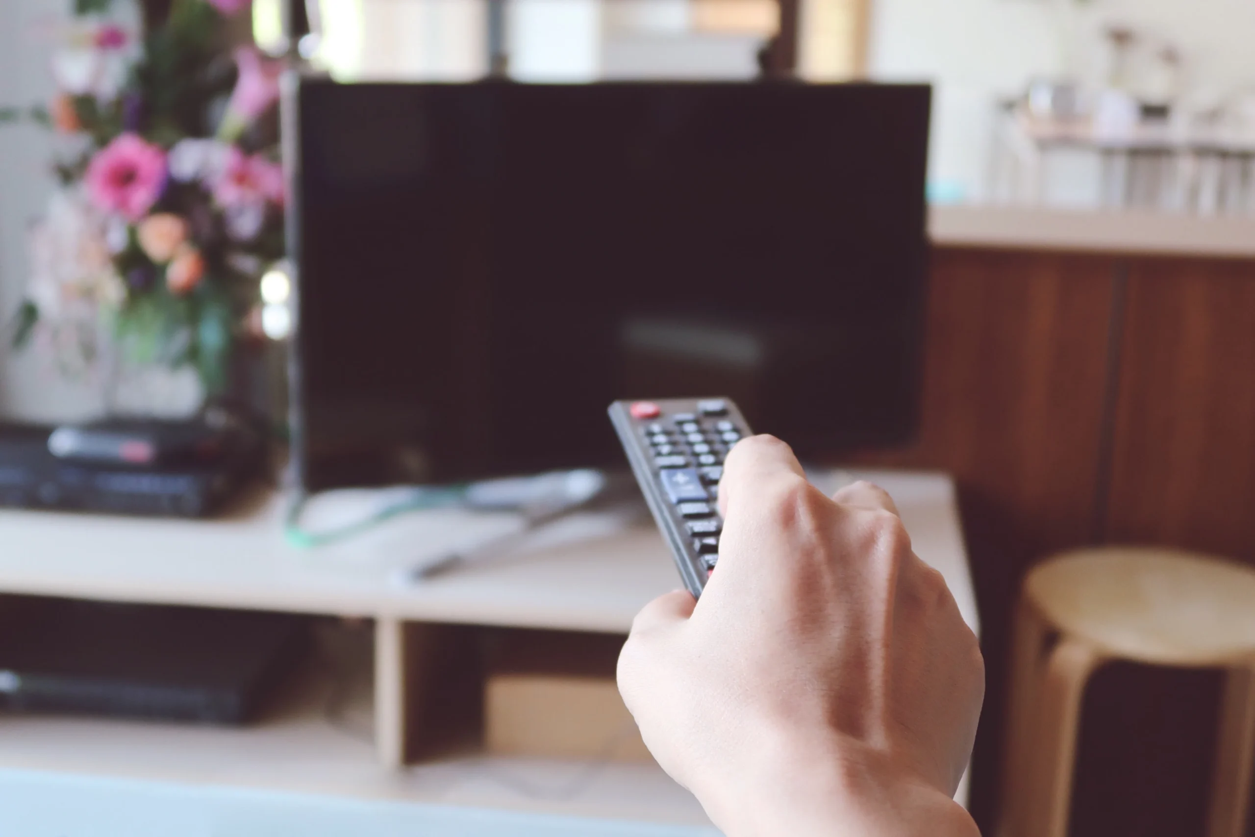 Pessoa segurando um controle remoto em direção a uma televisão desligada em uma sala de estar.